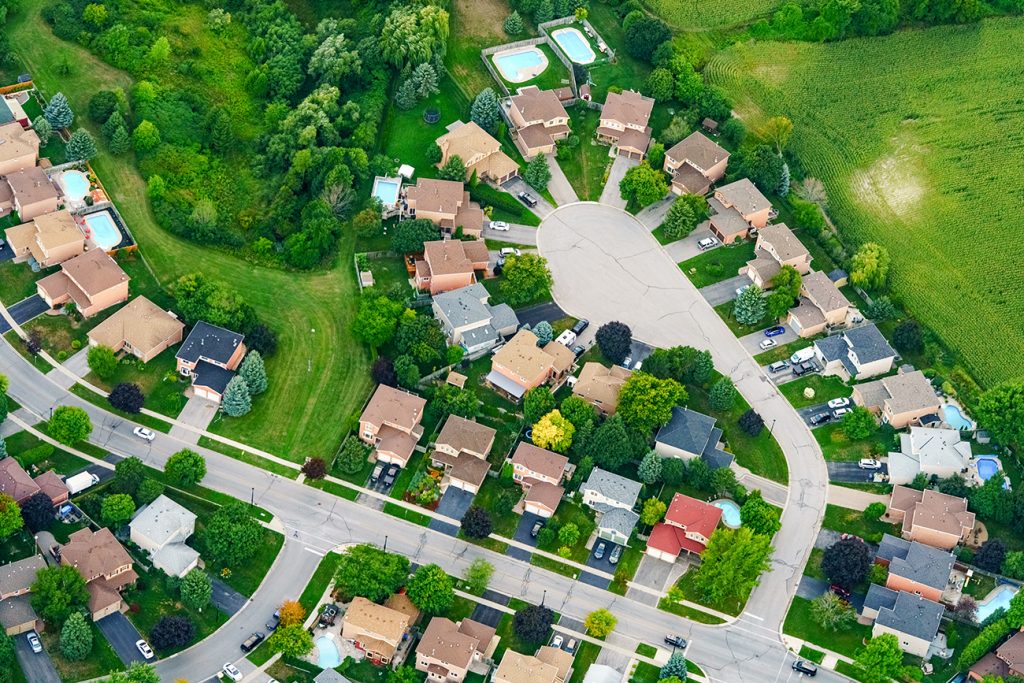 Aerial view of houses in residential suburban neighborhood surrounded by green grass and land.